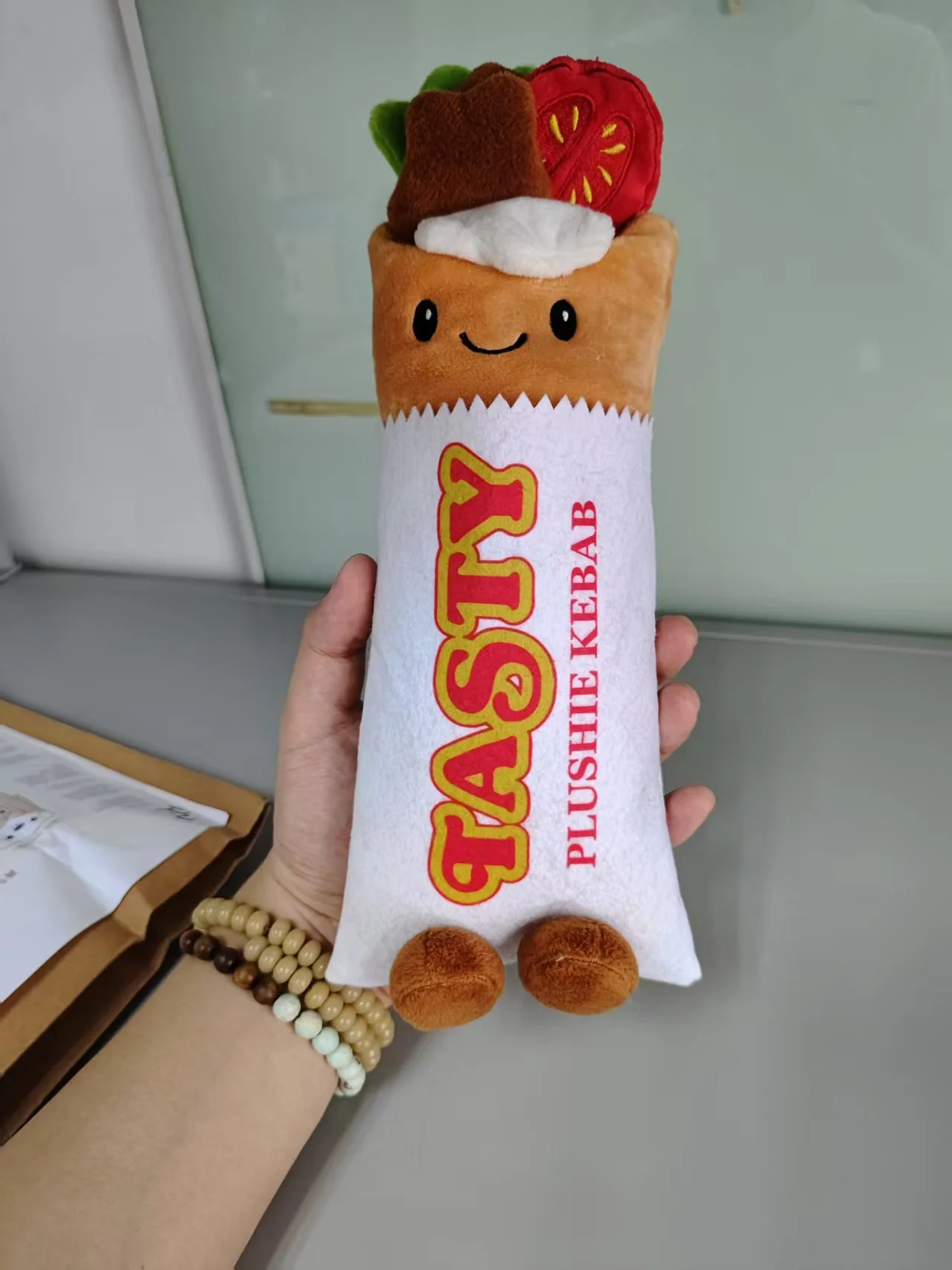 A large kebab-wrap plush sample held in a hand, showing the tomato and vegetable toppings and body graphics